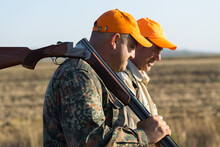 Duck Hunters With Shotgun Walking Through A Meadow.