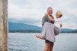 © Rob and Julia Campbell/Stocksy - Mature couple looking at camera near lake - man holding woman in arms