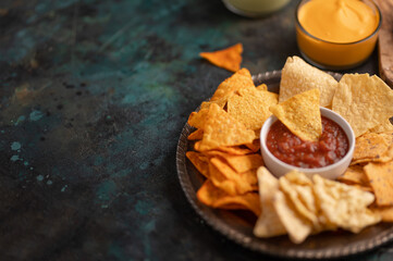 Wall Mural - The plate with tortilla nachos and souses are in the corner of photo. Dark background. Fast food concept. Tasty tortilla chips. Unhealthy food.