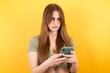Portrait of crazy impressed Caucasian woman wearing green shirt standing against yellow wall use cell phone reads incredible news on social media information stare, screams wow omg wear stylish outfit