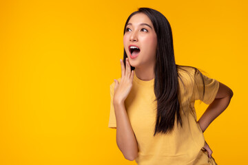 Wall Mural - Pretty girl gets surprised when look at copy space. Surprised happy beautiful asian woman looking copy space in exciting. Isolated on yellow background