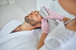 © Svitlana - Beautician in sterile gloves treating male skin with laser device