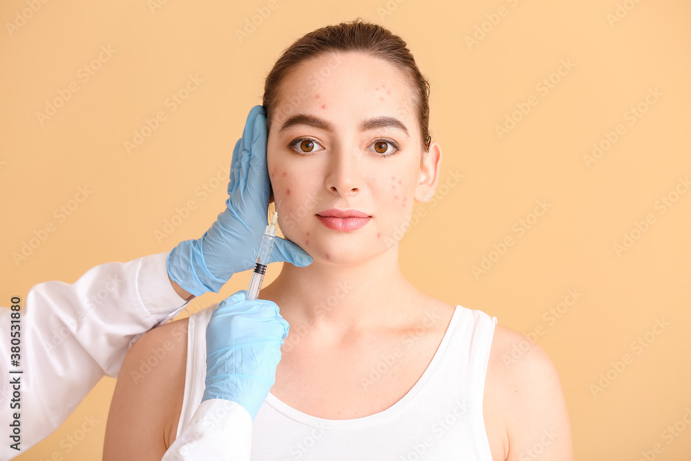 Young woman with acne problem receiving injection in her face against color background
