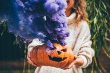 Woman Holding Halloween Pumpkin. Halloween Orange Pumpkin Smoking With Purple Smoke.