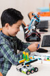 © LIGHTFIELD STUDIOS - Selective focus of asian schoolboy holding building block near robots in classroom