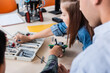 © LIGHTFIELD STUDIOS - Selective focus of teacher sitting near schoolkids modeling robot in classroom