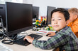 © LIGHTFIELD STUDIOS - Selective focus of asian schoolboy looking at camera while using computer in classroom