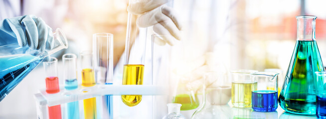 Wall Mural - hand of scientist holding flask and pouring sample to test tube in chemical laboratory background, s
