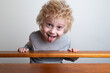 © somemeans - Funny boy with blond hair leaned over the banister and looks down. Child shows tongue and makes faces