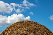 Round Hay Bales. Selective Focus On A Round Straw Hay Bale On A Agriculture Field Against A Blurred Blue Cloudy Sky Background. Harvesting In Autumn.
