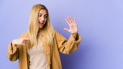 Young blonde woman isolated on purple background smiling cheerful showing number five with fingers.