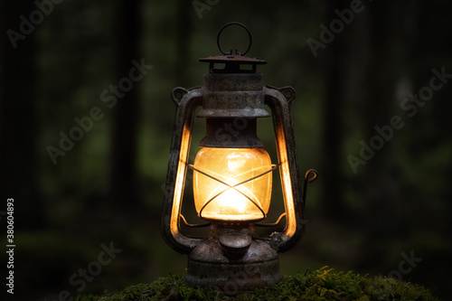 Old vintage lantern lit in the darkness close up. Blurred background image of a glowing lantern.