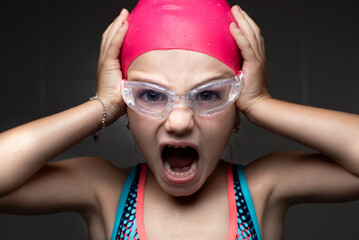 Closeup portrait of a little scared swimmer girl with swimming goggles and a pink bath cap.