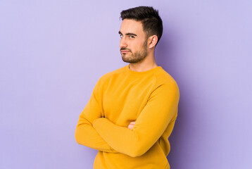 Wall Mural - Young caucasian man isolated on purple background suspicious, uncertain, examining you.