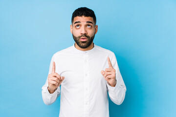 Wall Mural - Young latin man against a blue  background isolated pointing upside with opened mouth.