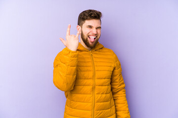 Wall Mural - Young man isolated on purple background showing rock gesture with fingers