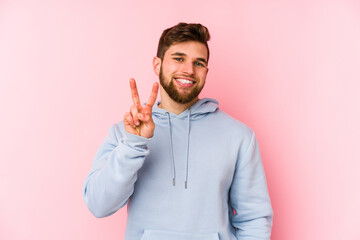 Wall Mural - Young caucasian man isolated on pink background showing victory sign and smiling broadly.