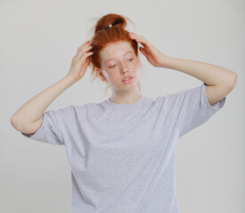 Portrait of tender redhead girl wearing her hair in bun with healthy freckled skin, serious or pensive expression. Caucasian woman model with ginger hair posing indoors in oversize shirt