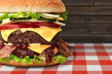 Hamburger On Red White Checked Tablecloth, Vichy Pattern Against Rustic Wooden Wall. Huge Cheeseburger Or Beef Burger With Bbq Meat Patty, Lettuce, Tomato, Onion, Roasted Bacon On Vichy Tablecloth.