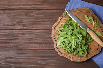 Cutting board with fresh arugula leaves and knife on wooden table, flat lay. Space for text