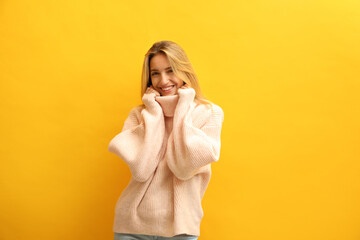 Wall Mural - Beautiful young woman wearing knitted sweater on yellow background