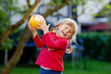 Wall Mural - Little adorable toddler girl playing with ball outdoors. Happy smiling child catching and throwing, laughing and making sports. Active leisure with children and kids.