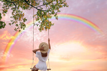 Dream World. Young Woman Swinging, Rainbow In Sunset Sky On Background