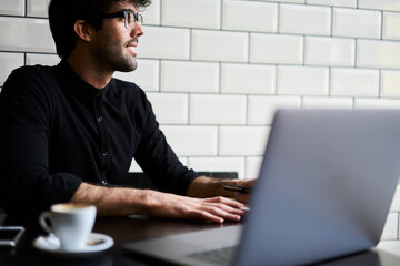 Wall Mural - Cheerful ethnic man taking notes at laptop in cafe