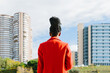 © MyMicrostock/Stocksy - Back view of calm black woman in red jacket looking at city