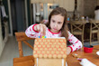 © Jakob Lagerstedt/Stocksy - Cute young girl in Santa Claus pajama making decorating a gingerbread house