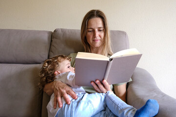 Mother breastfeeds her child while reading a relaxed book.