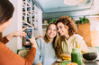 © MyMicrostock/Stocksy - Female friends taking pictures with smartphone in cafe