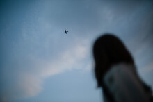 Silhouette Of Girl Looking At The Plane Flying At The Sunset Sky