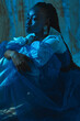 © Julie Meme/Stocksy - Photo of a black girl sitting in a fashionable outfit and golden earrings in the blue light at the studio