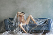 © Ivan Ozerov/Stocksy - concept photo. The girl is lying under a cellophane film on the sofa