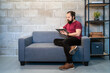 © Alvaro Sanchez/ADDICTIVE STOCK - Full body of focused young bearded male freelancer in casual outfit sitting on sofa and using tablet while working on project in contemporary loft workspace
