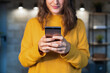 © Alvaro Sanchez/ADDICTIVE STOCK - Cropped unrecognizable happy young female in casual outfit using mobile phone while standing on modern loft room