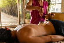 Cropped Unrecognizable Female Therapist With Bowl Pouring Oil On Back Of Unrecognizable Customer During Ayurvedic Healing Procedure In Salon