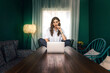© Luis Gomez/ADDICTIVE STOCK - Full length of positive young female in casual outfit using laptop while sitting on top of wooden table in cozy creative apartment
