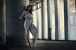 © Luis Gomez/ADDICTIVE STOCK - Full body of calm young female in stylish gray jacket and pants leaning against concrete column and looking at camera while standing in hall of contemporary building