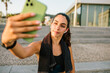 © Luis Tenza/ADDICTIVE STOCK - Young slim female in sportswear with earbuds and fitness tracker taking selfie on mobile phone while standing on street after training