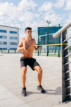Focused Shirtless Male Athlete Doing Exercises With Elastic Band During Training In City In Summer