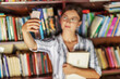 © Dusan Petkovic - Young beautiful brunette in dress and with eyeglasses holding a book and taking selfie while standing in library. Selective focus on hand.