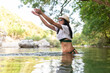 © Sergio Victor Vega/ADDICTIVE STOCK - Carefree female traveler standing in calm water of pond and enjoying summer vacation in forest