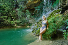 Serene Female In Bikini Leaning On Rock And Enjoying View Of Amazing Waterfall In Forest