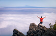© Javier Martinez/ADDICTIVE STOCK - Back view of anonymous male traveler standing with outstretched arms on rocky hill in highlands and enjoying amazing view of clouds