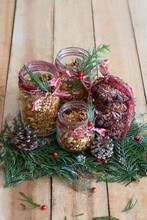 Glass Jars Filled With Granola And Decorated With Green Herbs And Red Berries Arranged On Wooden Table With Pine Cones For Christmas Celebration