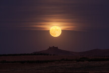 Bright Yellow Moon Glowing On Night Sky Over Distant Castle And Fields In Countryside