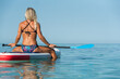 © Victor Prieto/ADDICTIVE STOCK - Back view of fit female surfer sitting on surfboard with paddle and relaxing during training in calm sea in summer