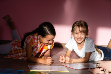 Wall Mural - family, leisure and childhood concept - happy sisters lying on floor and doing homework at home